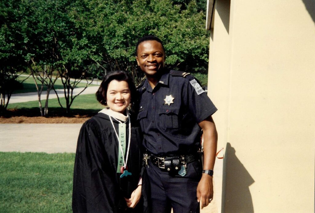 A male police officer in uniform takes a photo with a woman in her graduation robe.