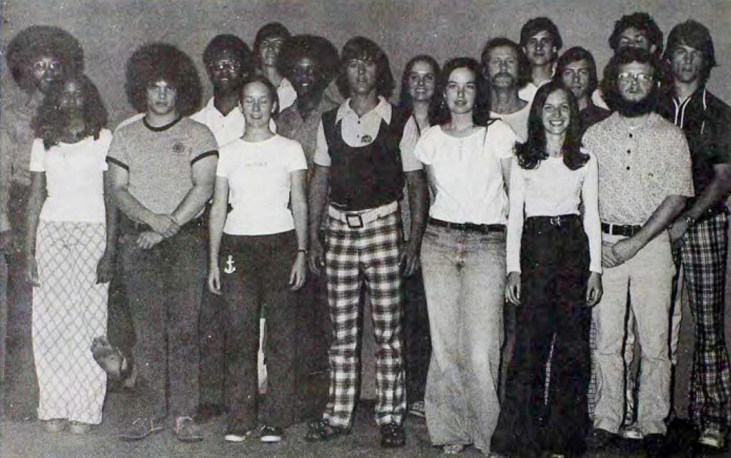 A large group of students in 70s attire stands to pose for a photo.