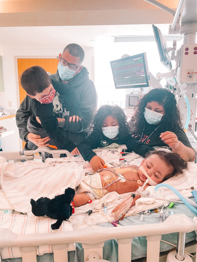 two parents and two kids next to a baby in a hospital bed.