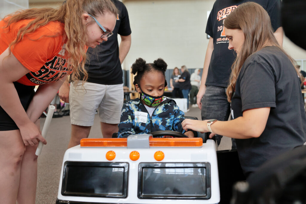 A child sits in a toy fire truck while four Mercer team members inspect the car.