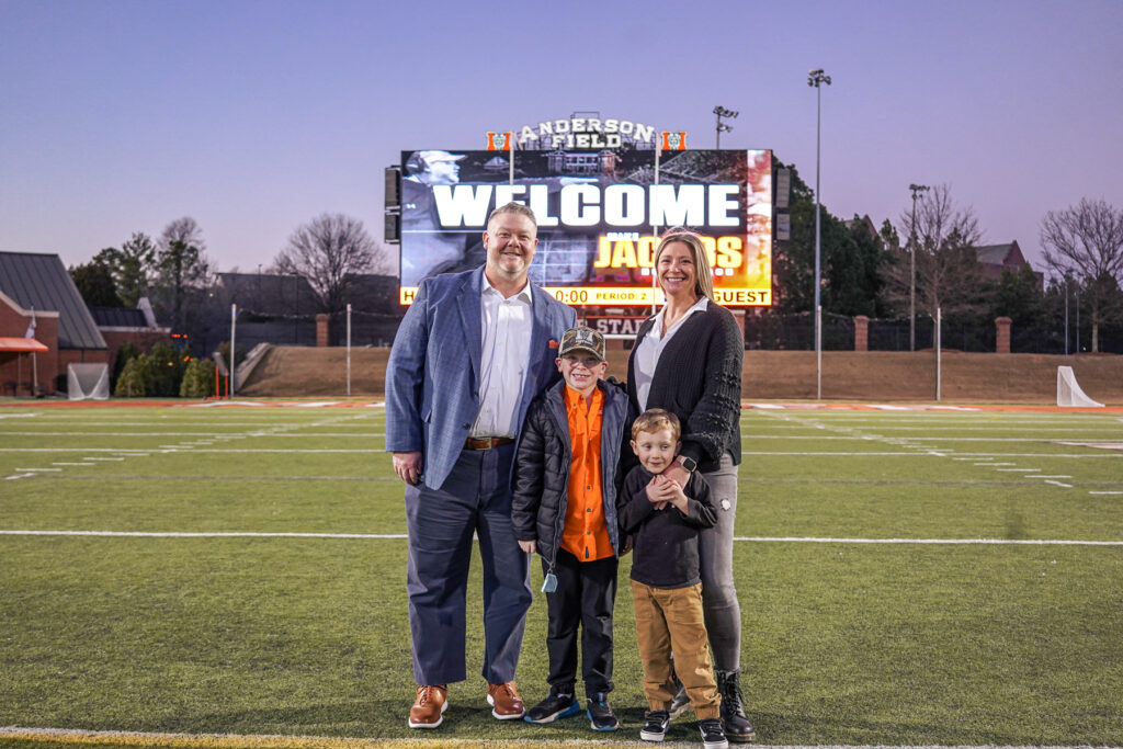 a man, woman and two kids stand on a football field with a scoreboard behind them