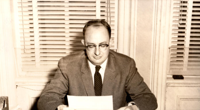 Dr. Malcolm Lester’s liberal arts legacy lives on through lecture series | Mercer Legends A black and white photo of a man in a suit reading papers at a desk.