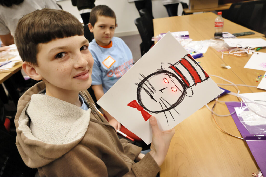 a middle school boys holds up a drawing of the cat in the hat with glowing red eyes