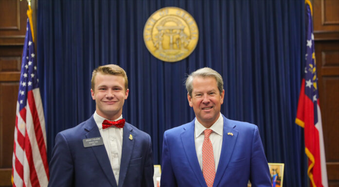 Student gets firsthand look at inner workings of government at Georgia State Capitol two men in suits stand next to each other in front of a large wooden desk with the Georgia state seal hanging behind them