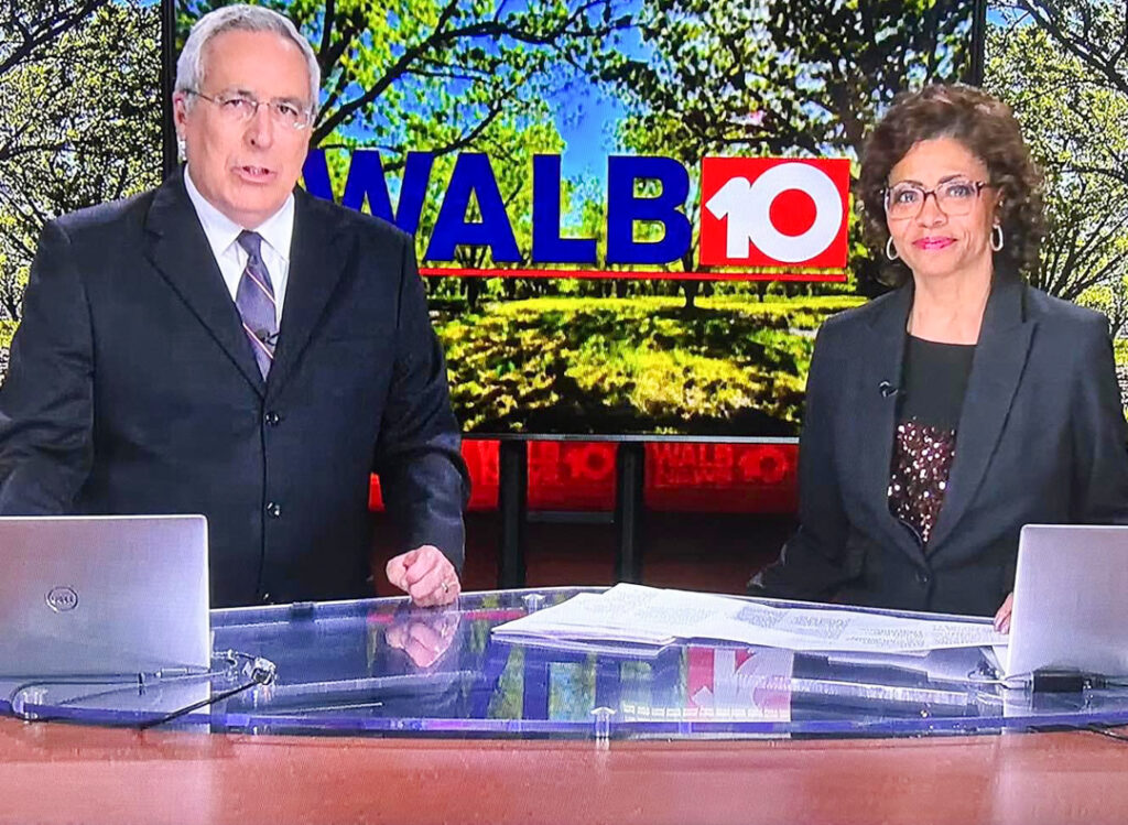 a man and woman sit behind a desk in front of a screen that says WALB 10