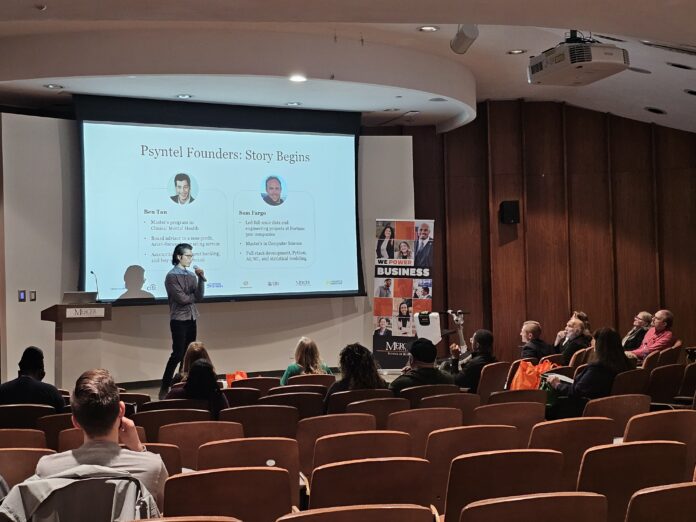 Benjamin Tan stands on stage in front of large projection screen presenting to audience. The screen says: Psyntel Founders: Story Begins, shows headshots of Ben Tan and Sam Fargo and provides some biographic information about each of them.