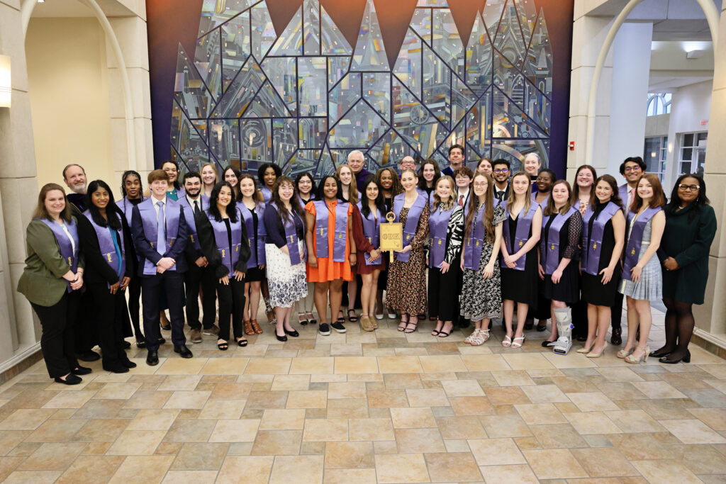 group of smiling faculty and students wearing Phi Beta Kappa sashes and holding plaque