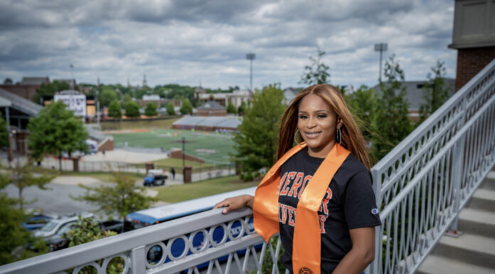 Graduate Spotlight: Breanna Smith-Jackson a woman wears a mercer t-shirt and orange stole. she is standing on a bridge overlooking the mercer football stadium