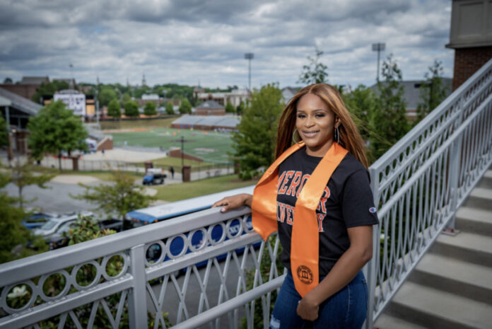 a woman wears a mercer t-shirt and orange stole. she is standing on a bridge overlooking the mercer football stadium