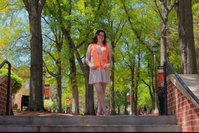 a woman stands on campus wearing an orange stole around her neck