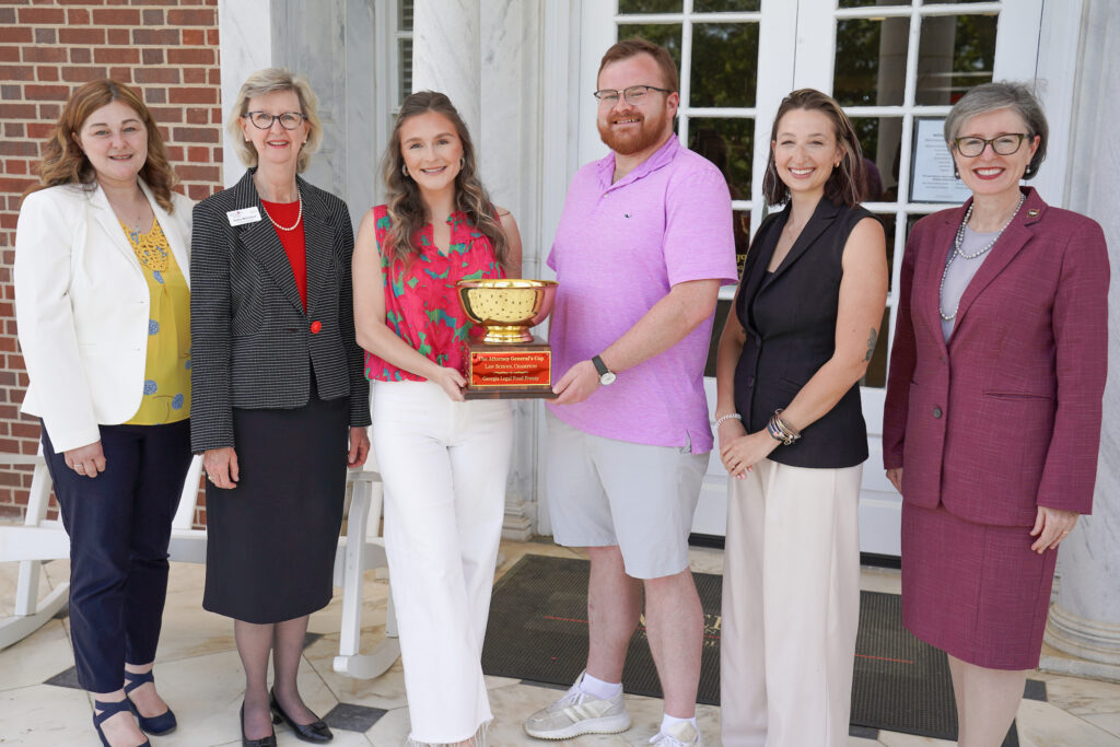 Mercer Law administration, Middle Georgia Food Bank administration, and two Mercer Law students stand on the law school's front porch holding the Law School Legal Food Frenzy Attorney General's Cup