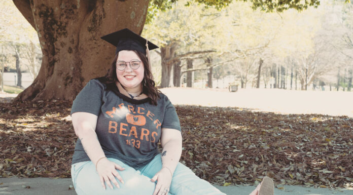 Graduate Spotlight: Madelyn Mauro female wearing a mercer shirt and graduation cap sits in front of a tree