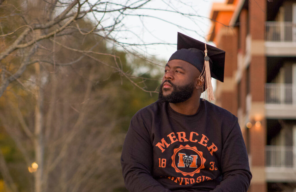 a man wearing a mercer sweatshirt and graduation cap looks off into the distance