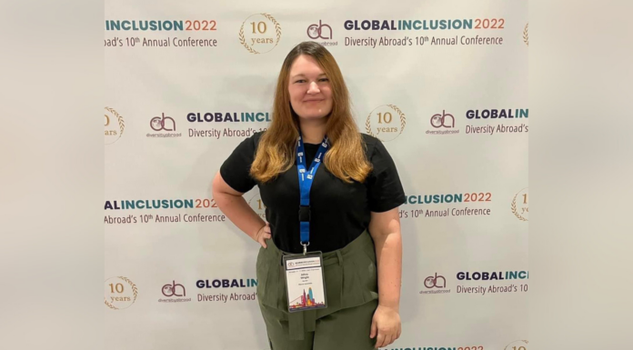 Mercer alumna builds on disability advocacy work as staff member, professor A woman with auburn hair wearing a black shirt and green pants stands in front of a backdrop that says Global Inclusion 2022 Diversity Abroad's 10th Annual Conference.