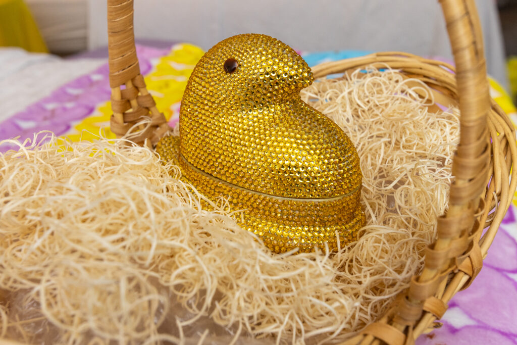 A sparkly gold ring box in the shape of a chick sits in an Easter basket with straw.