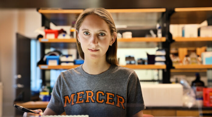 Goldwater Scholar immerses herself in biochemistry research at Mercer Sarah Boyer wearing a Mercer shirt looks at the camera. A lab is in the background.