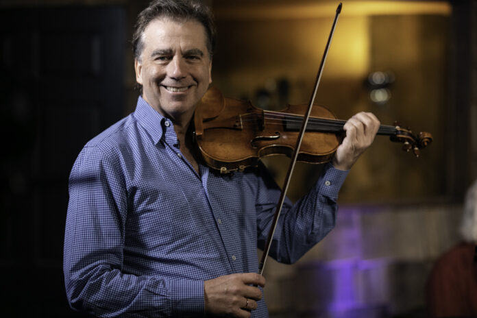 Robert McDuffie holds up a violin and bow, smiling.