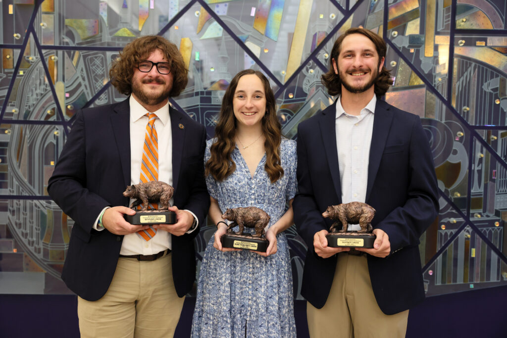 Two brothers and a sister, all Mercer students, stand together for a photo in front of a mirror mural while dressed up in nice attire.