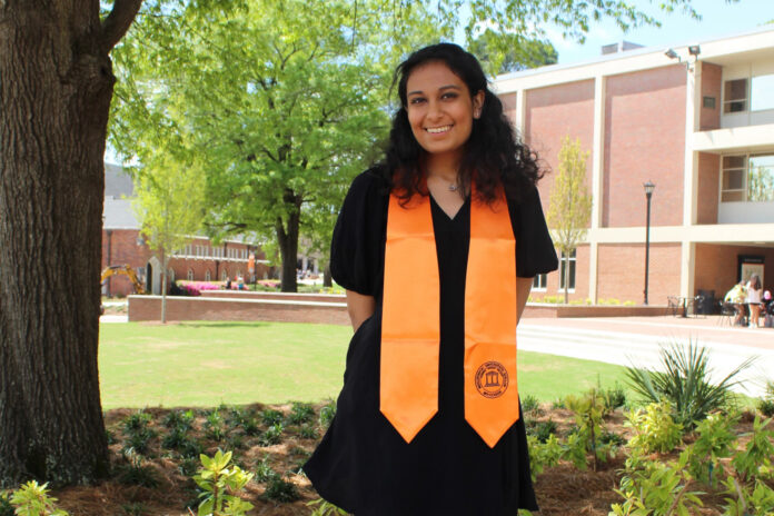 a woman wears a black dress and an orange stole around her neck