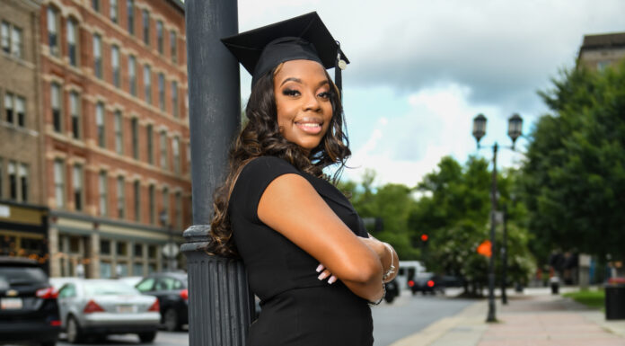 Graduate Spotlight: Alexis Stephens woman wearing a black dress and graduation cap leans against a pole in downtown Macon