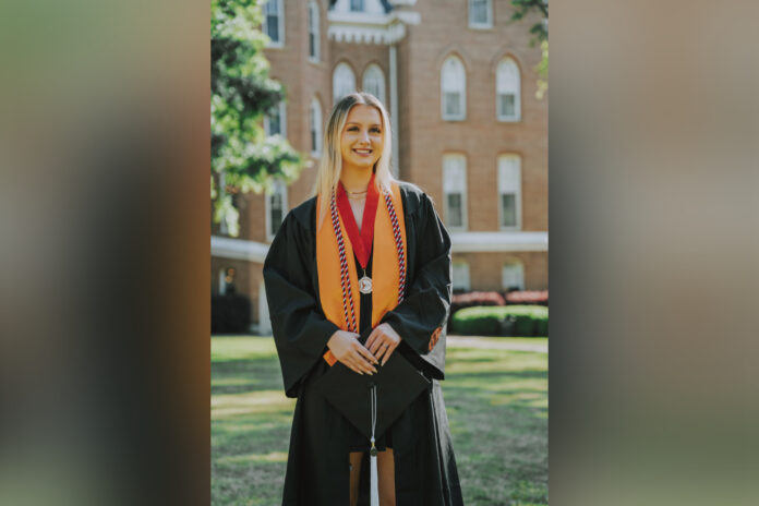 woman in graduation regalia stands in front of mercer's administration building