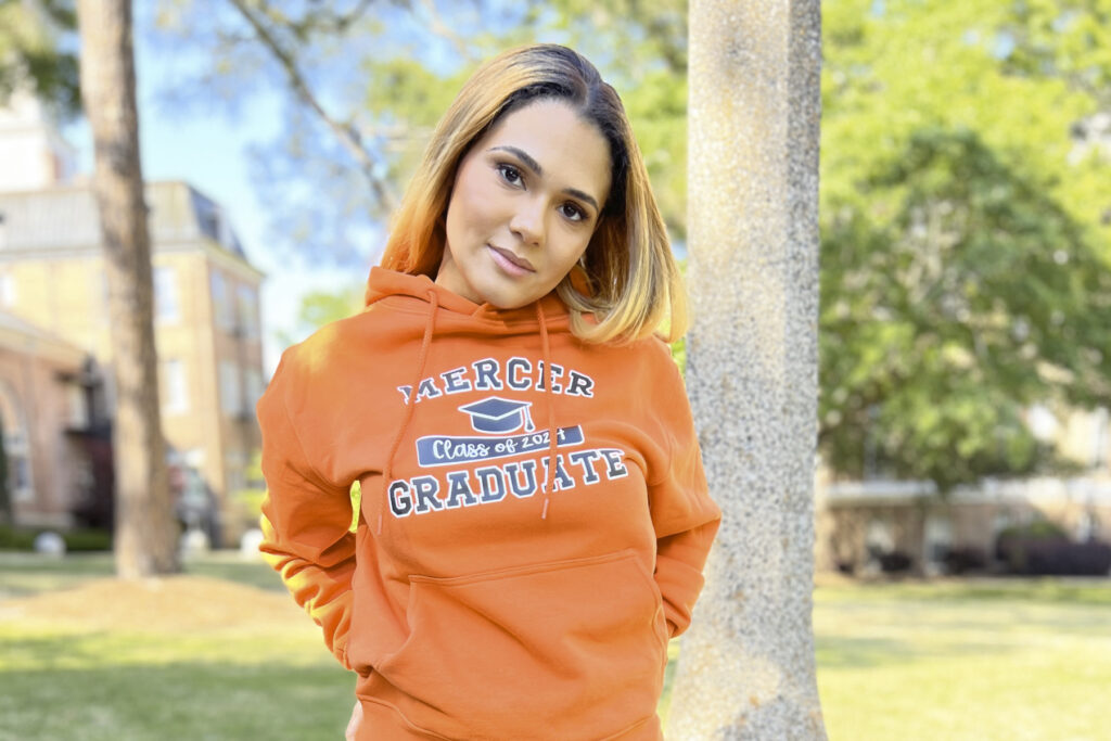 a woman wearing an orange sweatshirt that says Mercer Graduate on it.