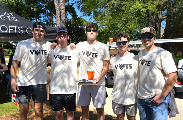 Five members of Mercer's men's lacrosse stand outside wearing matching white shirts that say 