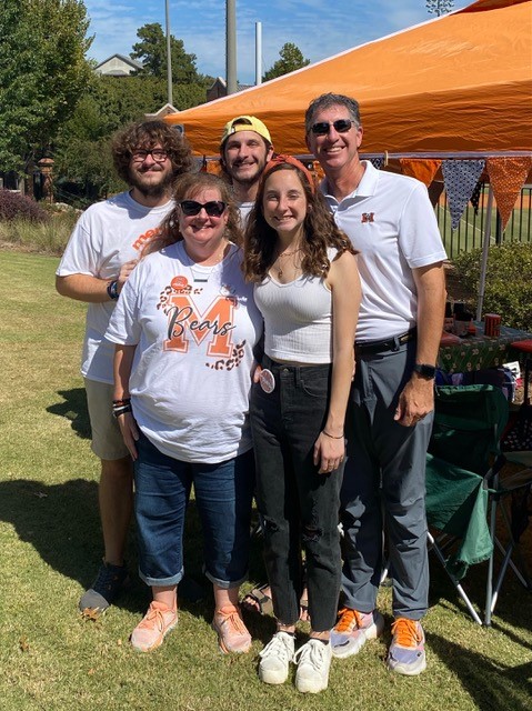 A family of three college students, a mother and a father wear Mercer shirts and pose for a photo during Homecoming.