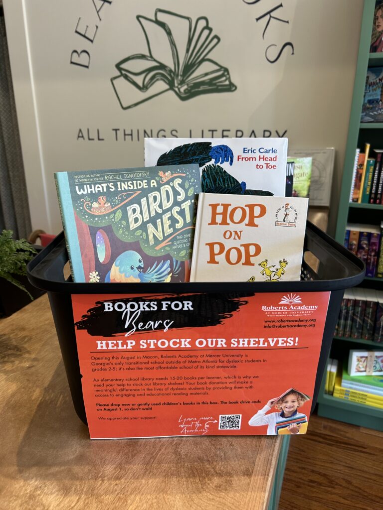 The photo depicts a collection box labeled "Books for Bears," which is part of a campaign to stock the library shelves at Roberts Academy at Mercer University in Macon, Georgia. The box contains children's books, including "What's Inside a Bird's Nest," "From Head to Toe" by Eric Carle, and "Hop on Pop" by Dr. Seuss.