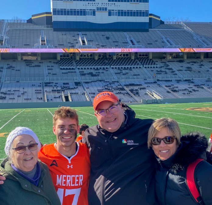 A male student in an orange jersey is pictured with his grandmother, father and mother with a stadium in the background.