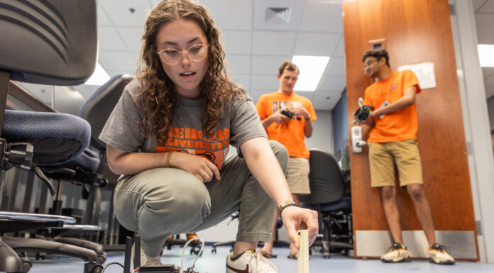 The future is in AI. A Mercer professor is preparing the next generation A Mercer University student crouches on the ground holding a small panel of wood in front of a small, wheeled robot.