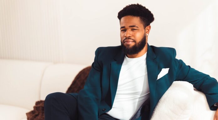 Alumnus lends viola talents to TV, film and other projects — including ‘Bridgerton’ A man in a dark blue suit and white shirt and pocket square sits on a white couch, with his arm draped over one side.