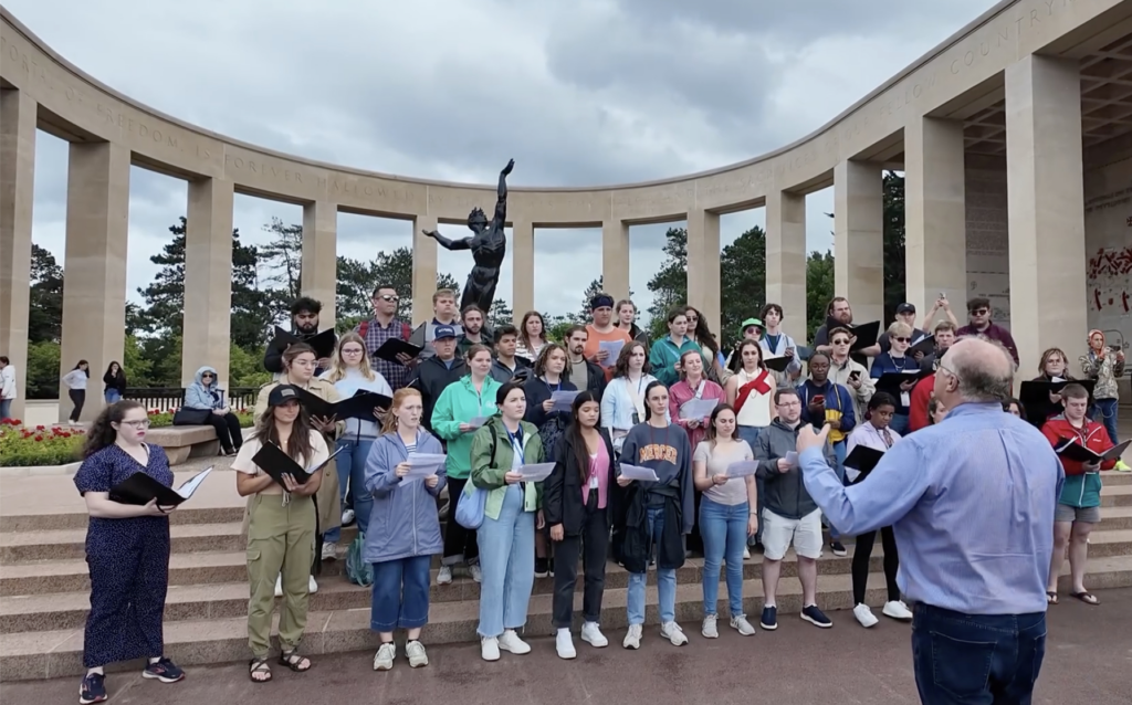 A choir sings in front of a memorial