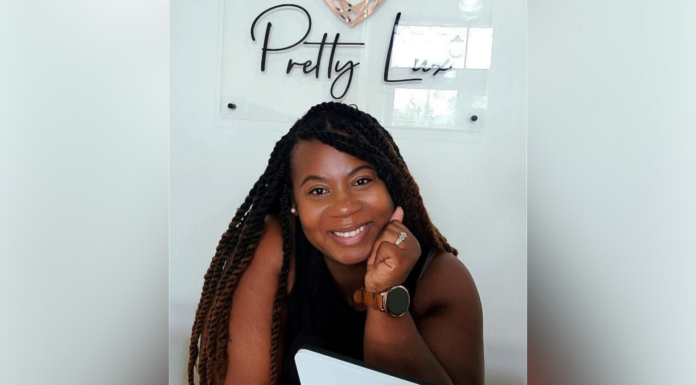 Mercer alumna offers candles, educational experiences at downtown shop A women smiling at the camera with their chin resting on their hand, sitting at a desk with a laptop. Behind them, a wall sign reads "Pretty Lux."