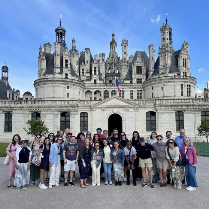 A group of students poses in front of a castle on a sunny day.