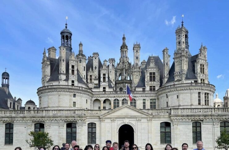 A group of students poses in front of a castle on a sunny day.