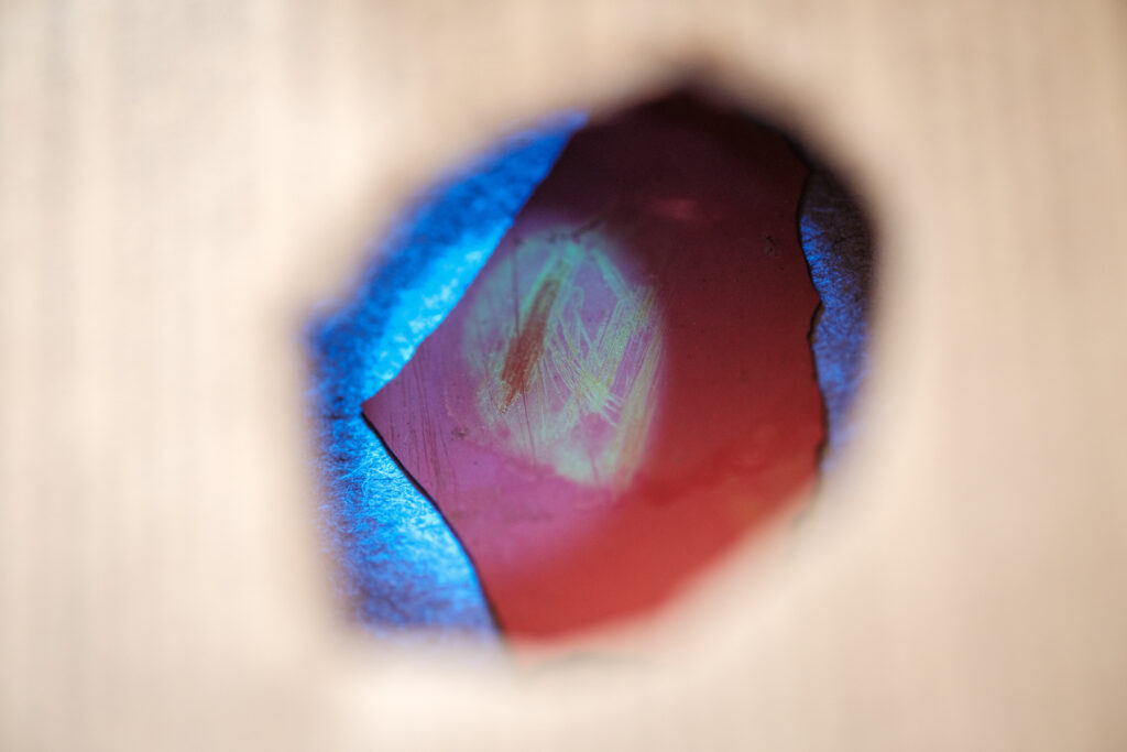 Close-up view of a paint sample glowing green under a black light as viewed from a small hole in a cardboard box.