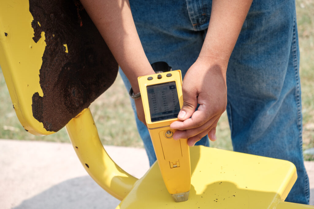 Close up of a person using a pXRF analyzer to test for lead on a piece of yellow outdoor exercise equipment.