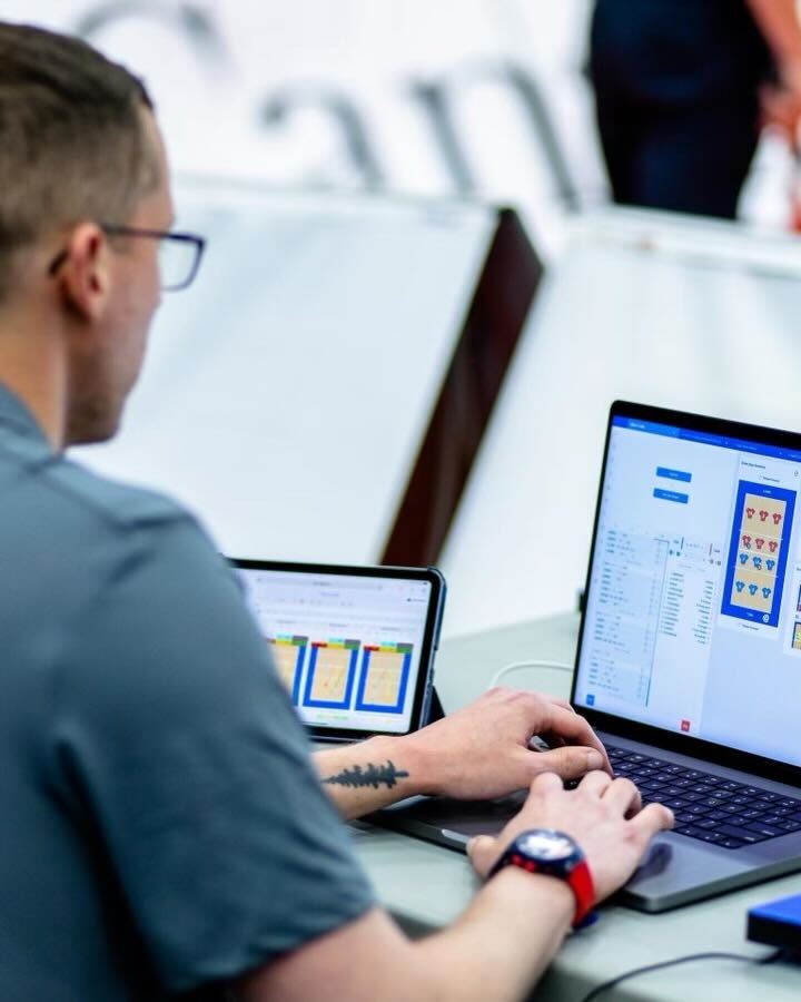 A man is shown sitting at a table working on a computer, with statistical software visible on the computer screen.