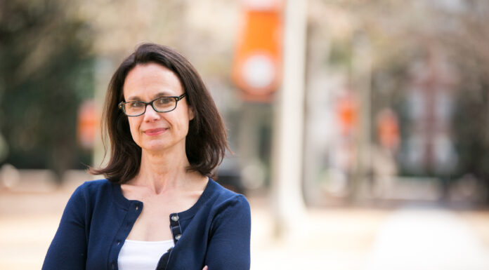 History professor awarded Loring Fellowship for Civil War research A woman with brown hair and glasses wears a white shit with a navy sweater over it. She stands with her arms crosses, with the Mercer University campus visible behind her.
