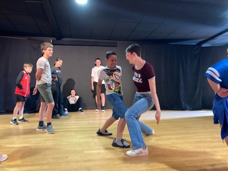 Children and Mercer students engage in a playful dance battle in a dance studio, with onlookers cheering and observing around them.