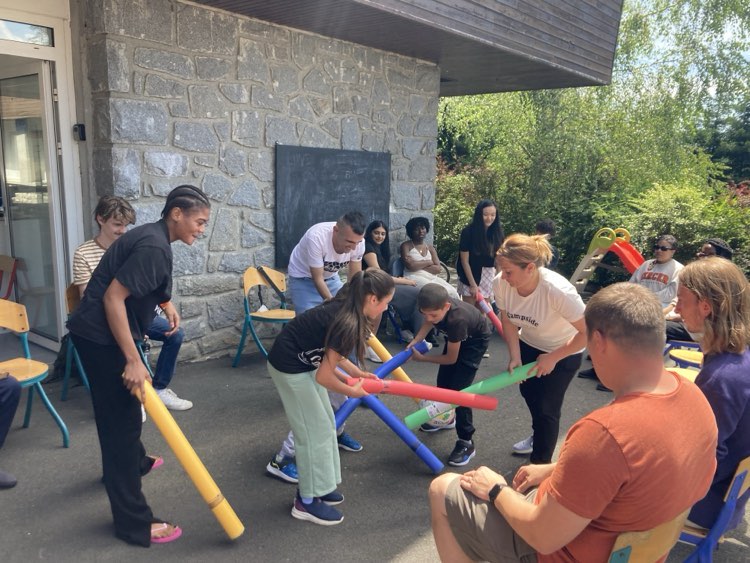 Group of people playing a game with colorful foam noodles in an outdoor community center setting.