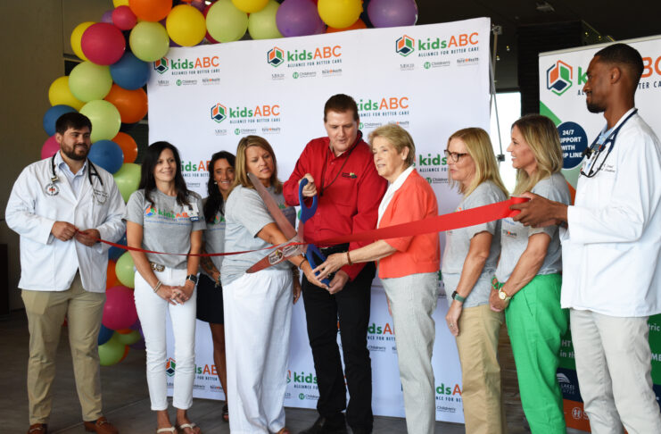 A group of people is gathered for a ribbon-cutting ceremony at the Mountain Lakes Medical Center. The backdrop features the 