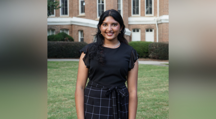 Student project leads to free period product dispensers on Macon campus A woman smiles for a photo while standing in front of a brick academic building and lush green grass. She wears a black blouse and black checkered skirt.