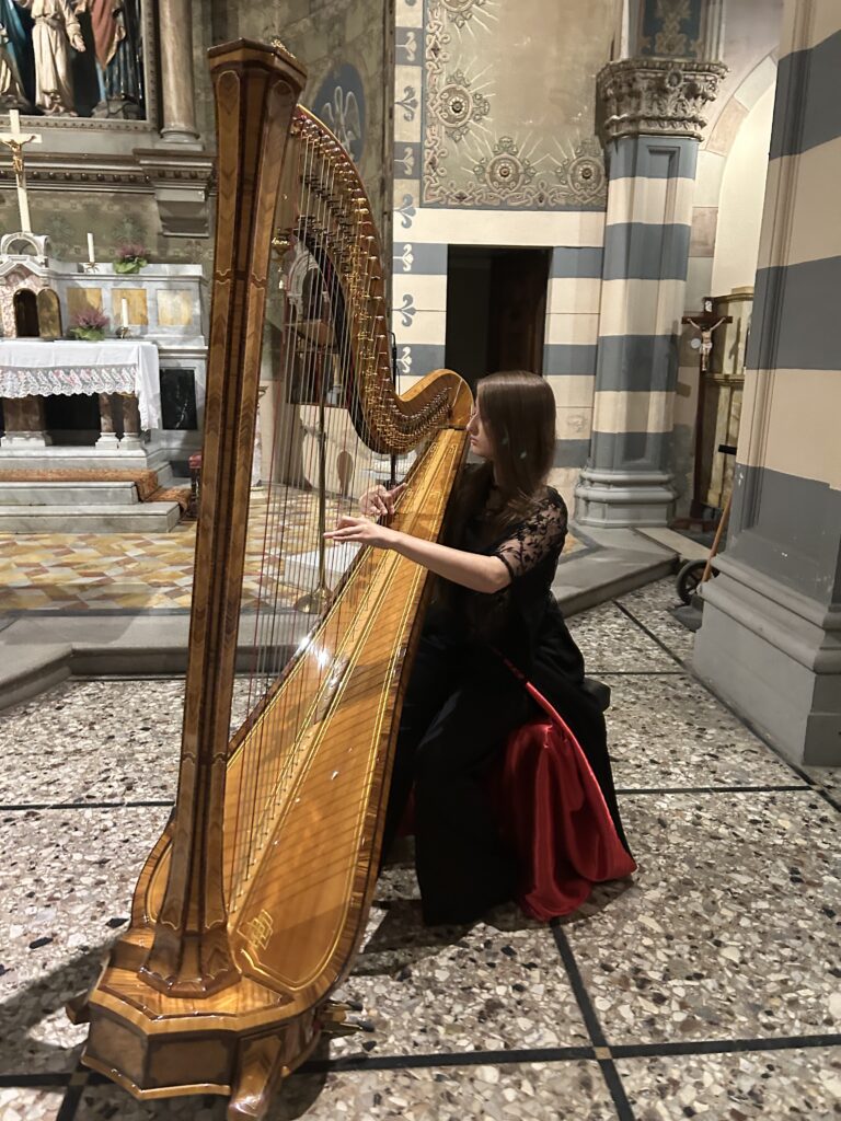 A woman in a black dress with lace sleeves plays the harp in an ornately decorated church.