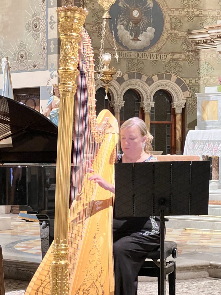 A woman playing a harp at a concert inside a richly decorated venue.