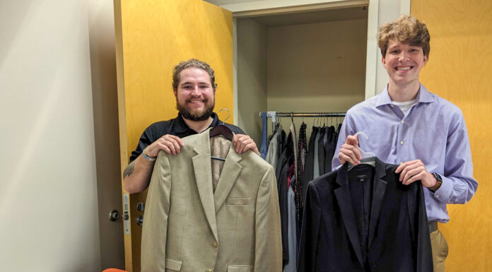 Business school launches clothing closet to give students access to blazers Two Mercer students smile while holding up blazers. More blazers are laid out on a desk in front of them, and others are hung in a closet behind them.