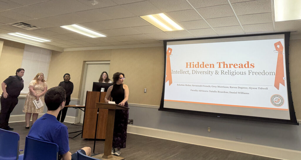 Presentation titled "Hidden Threads: Intellect, Diversity & Religious Freedom" in a conference room with several attendees and a speaker near the podium.