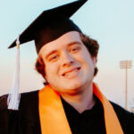 Headshot of Michael Mallard wearing a black graduation cap and gown. He has an orange stole around his neck.