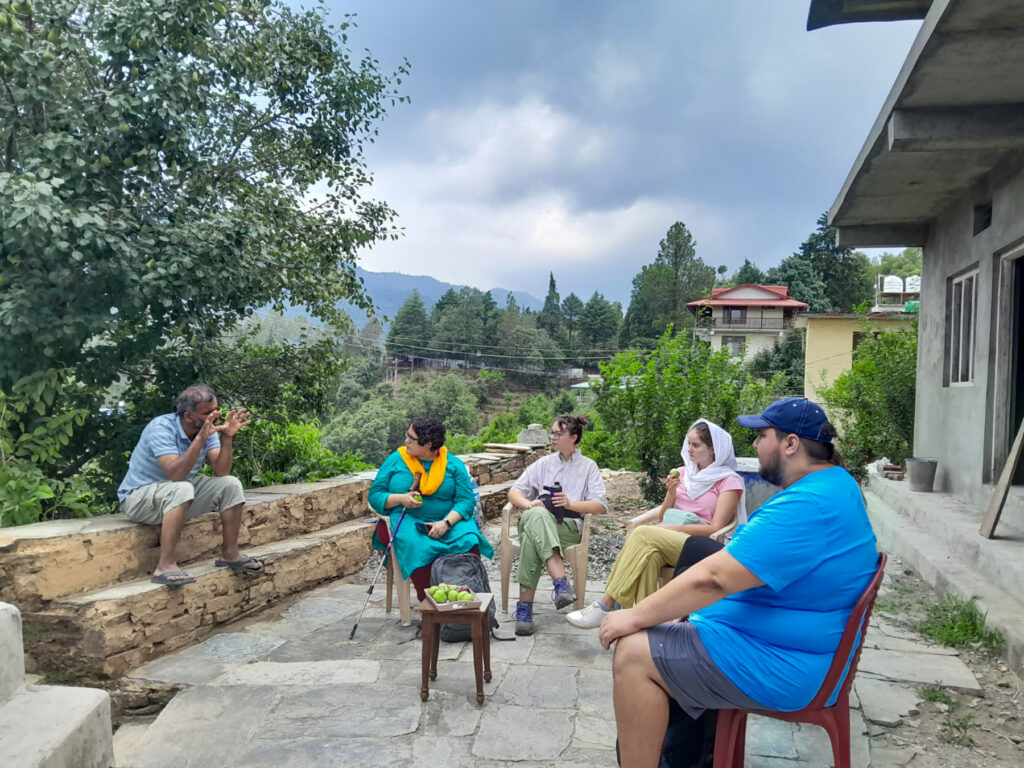 Three Mercer students, their professor and an Indian man sit in a semicircle on a stone patio. The man gestures with his hands while the others listen.